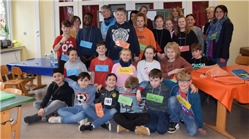 Mehrere Schülerinnen und Schüler stehen oder sitzen vor eine Tafel. 