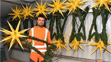 Ein Mann in oranger Bekleidung hält ein grün umwickeltes Gestell mit einem gelben Stern in der Hand.