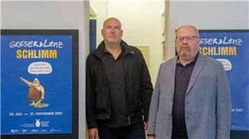 Die Zeichner Achim Greser (r) und Heribert Lenz stehen in einer Ausstellung.