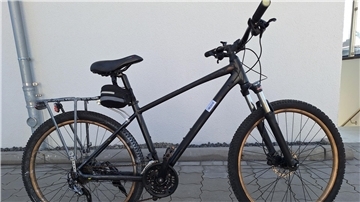 Ein schwarzes Fahrrad mit goldfarbenen Felgen steht vor einer weißen Wand. 