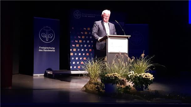 Ein Mann steht an einem Pult vor dem Blumen stehen.