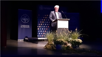 Ein Mann steht an einem Pult vor dem Blumen stehen.
