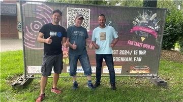 Drei Männer vor einem Festivalplakat.