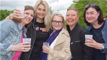 Fünf Frauen stehen eng beieinander, lächeln in die Kamera und halten Becher in der Hand. 
