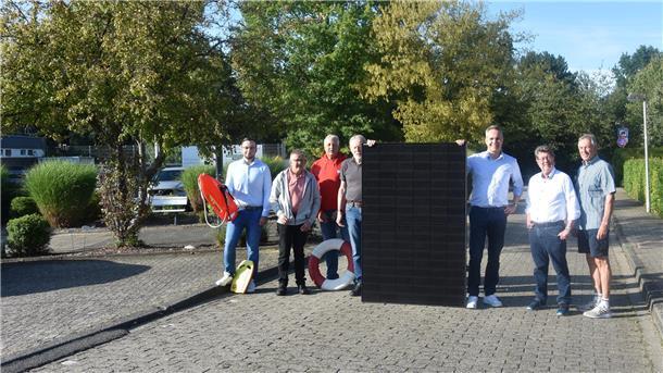 Sieben Männer stehen auf einer gepflasterten Straße und halten ein Photovoltaik-Modul in ihrer Mitte.