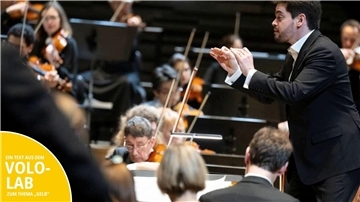 Ein Orchester mit Dirigenten spielt vor Publikum.