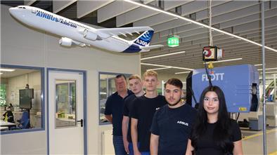 Vier Auszubildende und der Ausbildungsleiter stehen in der Werkshalle in einer Reihe. 