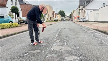 Dieter Allmers zeigt auf die Schäden, die sich aufgrund des starken Verkehrs auf der Atenser Allee gebildet haben.