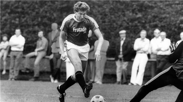 Ein Fußballer schießt den Ball am Torwart vorbei.