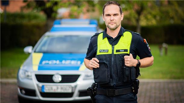 Ein Polizist steht vor seinem Dienstwagen