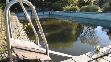 Ein blau gekacheltes Becken, in dem Wasser steht und im Vordergrund ist ein glänzender Metallbogen.