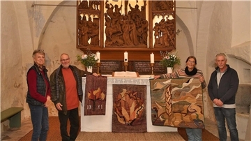 Im Altarraum der Padingbütteler Kirche stehen vier Personen mit drei handgewebten Paramenten
