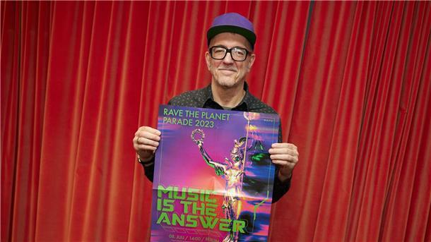 „Rave The Planet“ wird stattfinden Dr. Motte hält das Plakat zur jetzt doch stattfindenden Techno-Parade hoch.