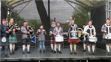 Die Happy German Bagpipers stehen auf einer Bühne und machen Musik.