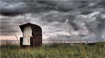 Dunkle Wolken über einem verlassenen Strandkorb.