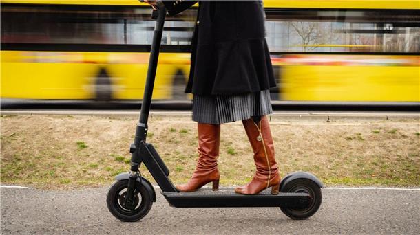 E-Roller-Verbot in Bussen: Das sagen die Verkehrsbetriebe Wesermarsch Frau fährt mit einem E-Tretroller, im Hintergrund ist ein vorbeifahrender Bus zu sehen.