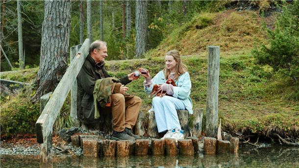 Ein Mann und eine Frau sitzen in einem Wald an einem Fluss. Edgar Selge als Helmut und Luna Wedler als Paula in einer Szene aus "Marianengraben": Das Kommunale Kino zeigt den Film am 19. März um 18 und 20.30 Uhr. Im März stehen vier weitere Filme auf dem Programm.