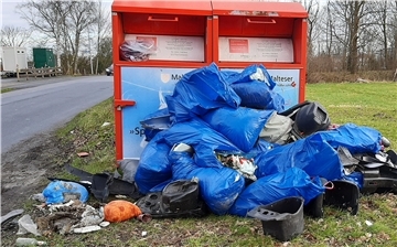 Mehrere Tüten mit Müll liegen vor zwei Altkleidercontainern.