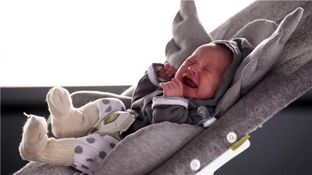 Ein Baby liegt in einer Kinderwippe und schreit.