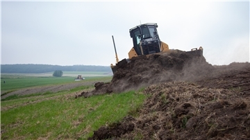 Ein Bagger schält den Mutterboden vom Deich ab. Anschließend wird er mit schwerem Kleiboden erhöht. Am Ende wird der Mutterboden wieder breitgefahren, damit das Gras schneller anwächst.