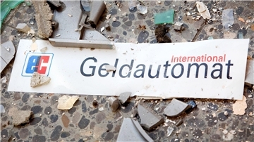 Das Schild eines Geldautomaten liegt zwischen Scherben und Trümmern auf dem Boden.