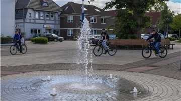 Drei junge Menschen fahren mit dem Fahrrad über einen Marktplatz.