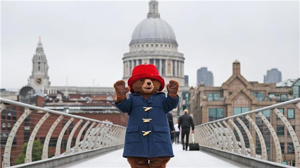 Ein Darsteller im Kostüm des Paddington-Bär  auf der Millenium-Brücke vor der Kuppel der St.-Pauls-Kathedrale in London.