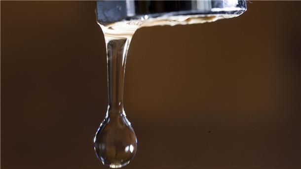 Nahaufnahme eines Wasserhahns, an dem ein Wassertropfen hängt. 