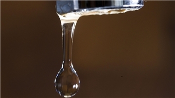 Nahaufnahme eines Wasserhahns, an dem ein Wassertropfen hängt. 