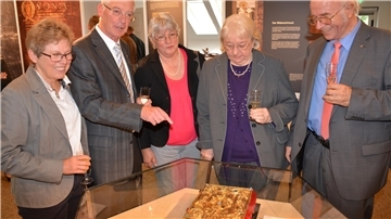 Eine Gruppe von Menschen steht vor einer Vitrine. Darin liegt der wertvollste Besitz des Rüstringer Heimatbundes in Nordenham: ein Faksimile des Krönungsevangeliars.
