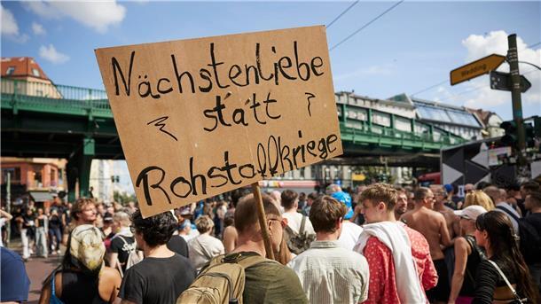 „Zug der Liebe“: Technofans tanzten durch Berlin Ein Feiernder trägt ein Schild mit der Aufschrift „Nächstenliebe statt Rohstoffkriege“ bei der Technoparade Zug der Liebe durch Berlin.