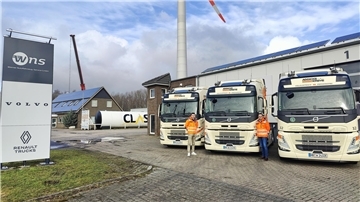 Zwei Männer stehen auf einem Lkw Hof vor drei Elektro-Lkws