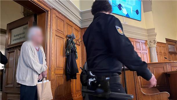 Alter Mann wird vom Justizbeamten auf seinen Platz geführt.