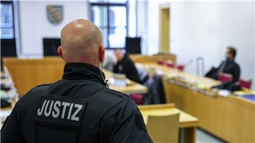 Ein Justizbeamter steht vor Prozessbeginn vor einigen Angeklagten im Landgericht Chemnitz.