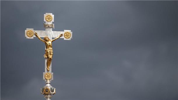 Christliche Geistliche fordern Ausbau der Suizidprävention Ein katholisches Kruzifix ist vor dunklen Wolken zu sehen.