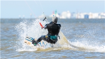Ein Kitesurfer fährt bei Norddeich durch das Wasser. An der Nordsee läuft der Tourismus langsam wieder an.