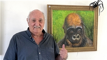 Ein älterer Mann mit schütterem grauen Haar und einem grauen Oberlippenbart steht vor einem Kunstwerk und zeigt mit seiner linken Hand auf das Gemälde - auf dem ist ein Affe (Gorilla?) zu sehen. Am oberen Rand des Gemäldes scheint eine schwarze Spinne (schwarze Witwe?) zu sitzen.