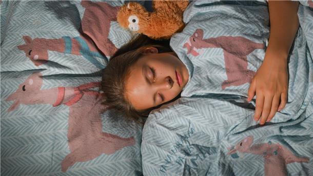 Schlummern oder lieber nicht? Ein Mädchen liegt eingekuschelt im Bett. Sich morgens aufzuraffen, fällt meist schwer. Fachleute aber raten vom Schlummern ab.
