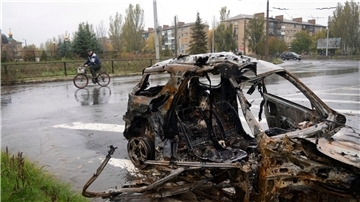 Ein Mann fährt in Bachmut mit seinem Fahrrad an einem Auto vorbei, das durch Beschuss zerstört wurde.