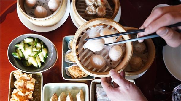 100 Jahre Chinarestaurants in Deutschland Ein Mann greift mit Essstäbchen nach Dim sum, gedämpften Teigtaschen, in einem Bambuskorb.