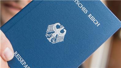 Ein Mann hält ein Heft mit dem Aufdruck „Deutsches Reich Reisepass“ in der Hand.
