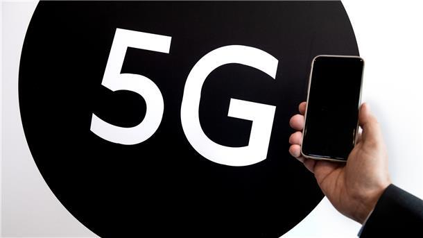Ein Mann hält ein Smartphone neben ein 5G-Plakat.