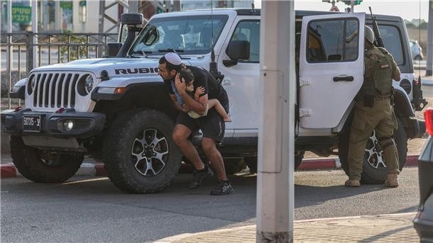 Deutsche von Hamas entführt - Evakuierungsflüge Ein Mann hält in Ashkelon ein Kind im Arm und sucht bei einem neuen Raketenangriff aus Gaza hinter einem Fahrzeug Deckung.
