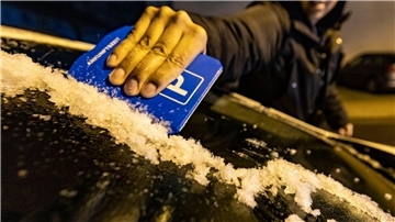 Ein Mann kratzt in Duisburg mit einer Parkscheibe die Eisschicht von der Windschutzscheibe seines Autos.