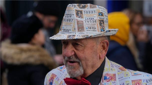 Ein Mann mit einem Anzug und Hut, der mit gedruckten Lottoscheinen verziert ist, steht vor dem berühmten Lotterieladen „Dona Manolita“ in der Innenstadt von Madrid.