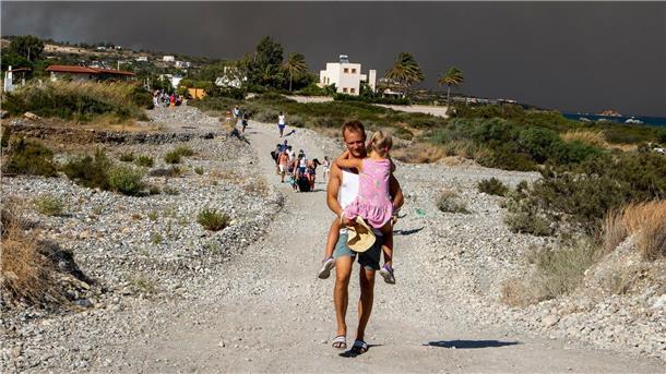 Griechische Feuerwehr: Brände größtenteils unter Kontrolle Ein Mann mit einem Kind auf dem Arm verlässt ein Waldbrandgebiet auf Rhodos.