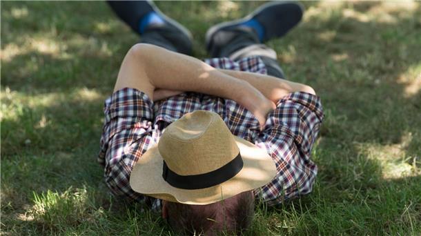 Hitze am Mittelmeer - und Siesta bald auch in Deutschland? Ein Mann mit einem Sonnenhut auf dem Gesicht liegt auf einer Wiese im Schatten und ruht sich aus.
