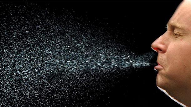 Ein Mann niest. Beim Niesen fliegen viele Tröpfchen durch die Luft. Auf diese Weise kann sich auch das neuartige Coronavirus Sars-CoV-2 verbreiten.