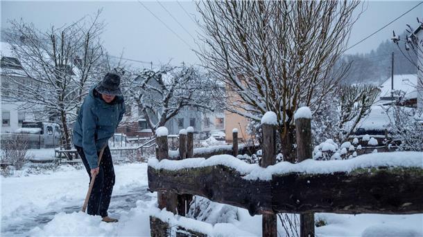 Ein Mann schaufelt in Kordel, Rheinland-Pfalz, Schnee von der Straße.