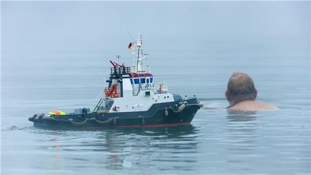 Ein Mann schwimmt neben einem Modellboot.
